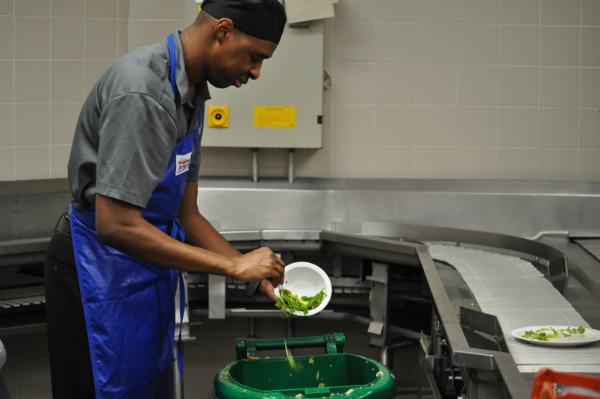 An employee behind the conveyer belt, scraping off leftover food from students’ plates.
